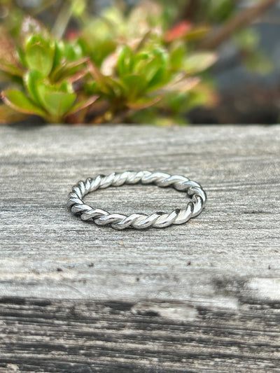 Silver braided ring on a wooden surface with blurred greenery in the background