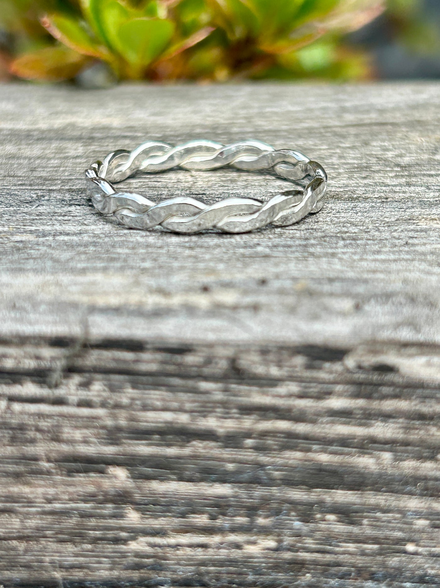 Silver braided ring on a wooden surface with greenery in the background