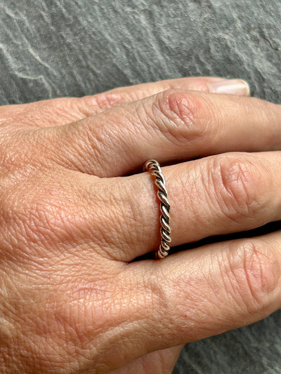 Hand wearing a silver twisted rope ring on a gray background