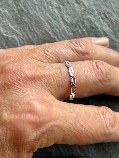 Hand wearing a silver braided ring on a gray background