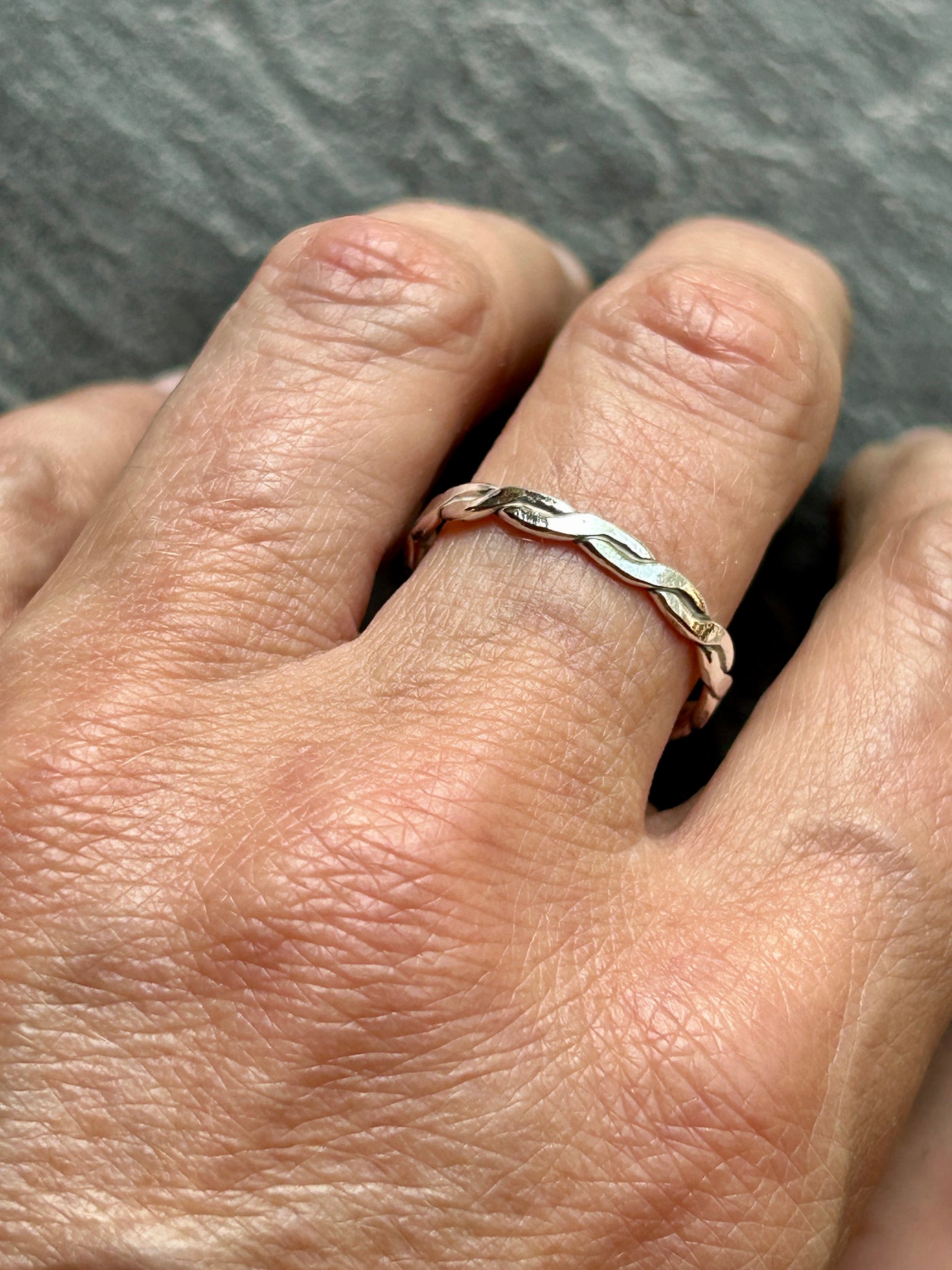 Hand wearing a silver braided ring on a gray background
