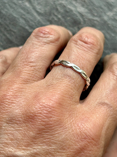 Hand wearing a silver braided ring on a gray background