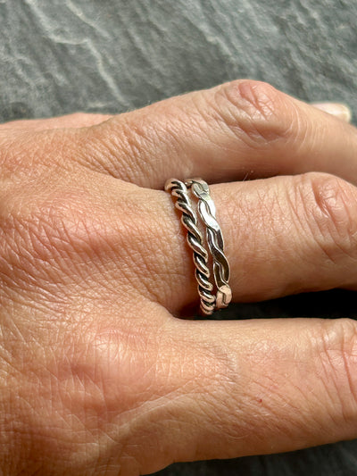 Silver braided ring on a finger with a gray background