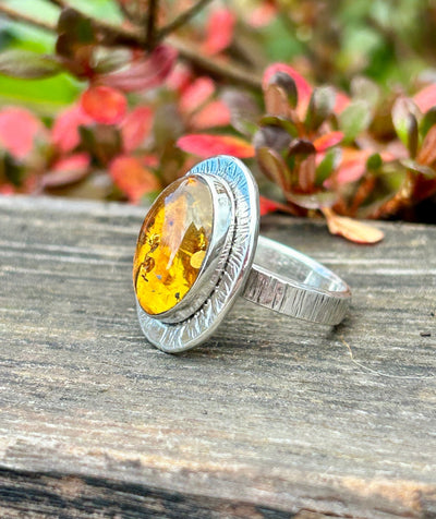 Silver ring with a amber stone on a wooden surface with blurred green and red foliage in the background