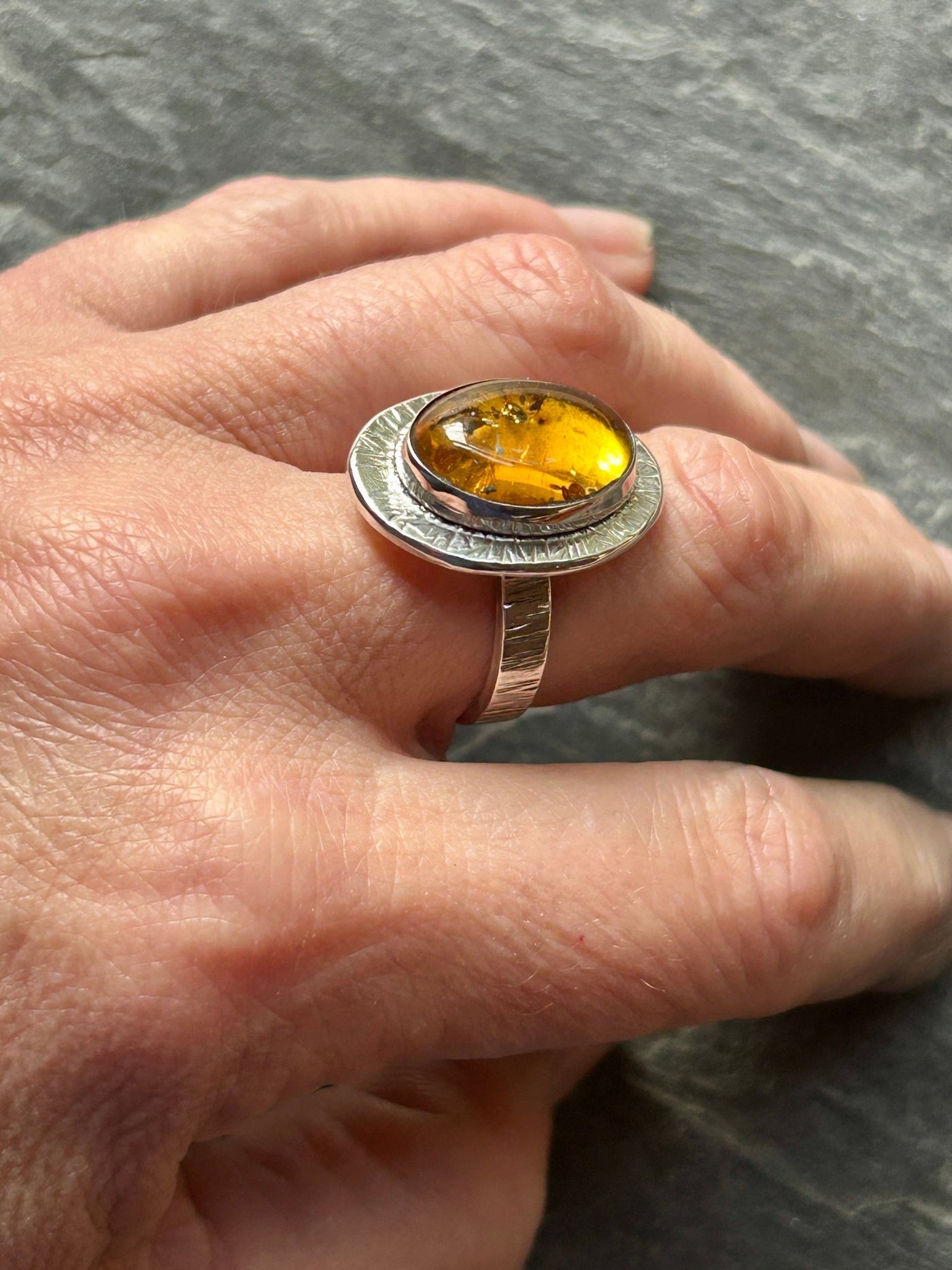 Ring with an amber gemstone on a finger against a gray background
