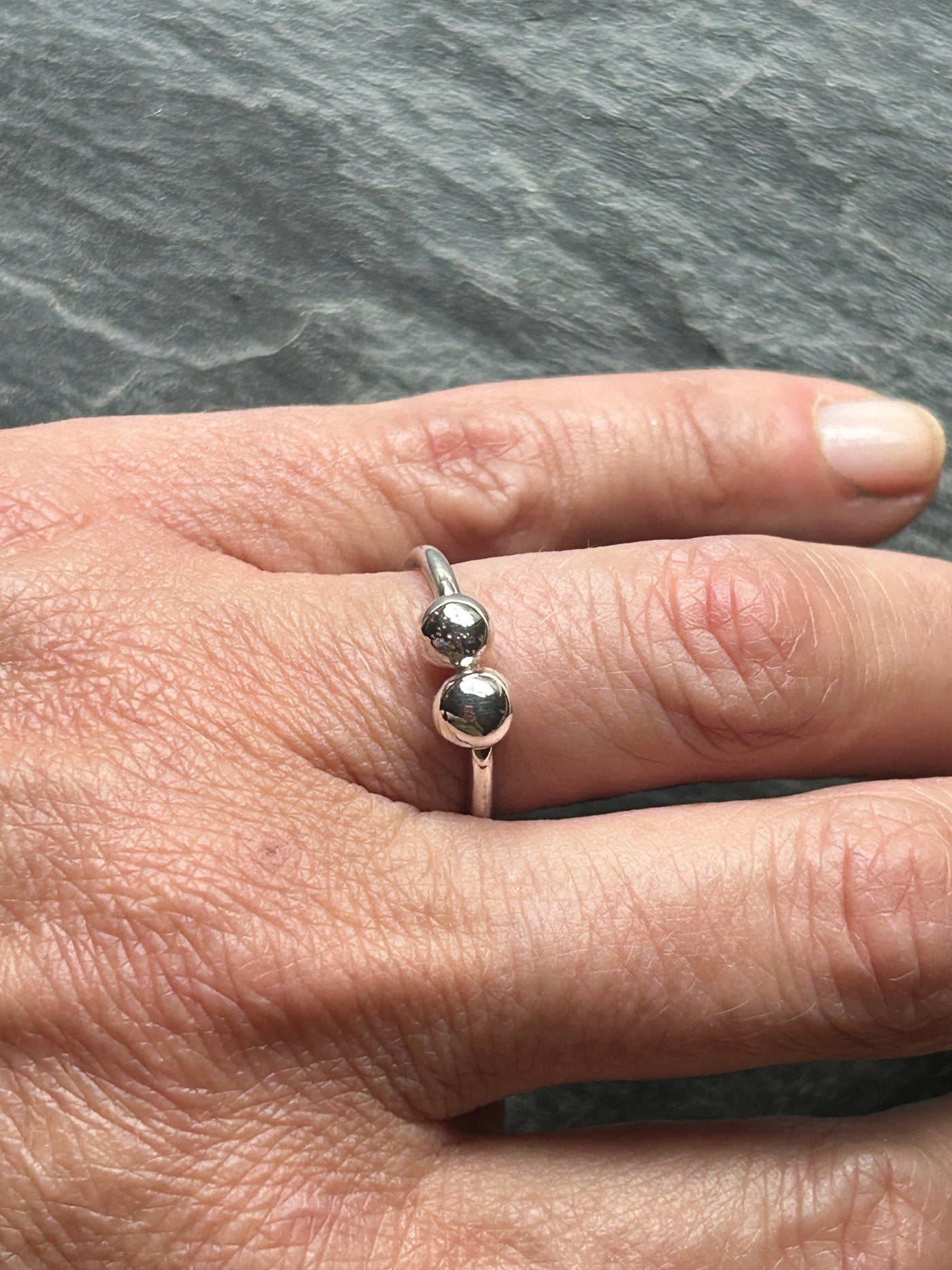 Silver ring with two balls on a hand against a grey background