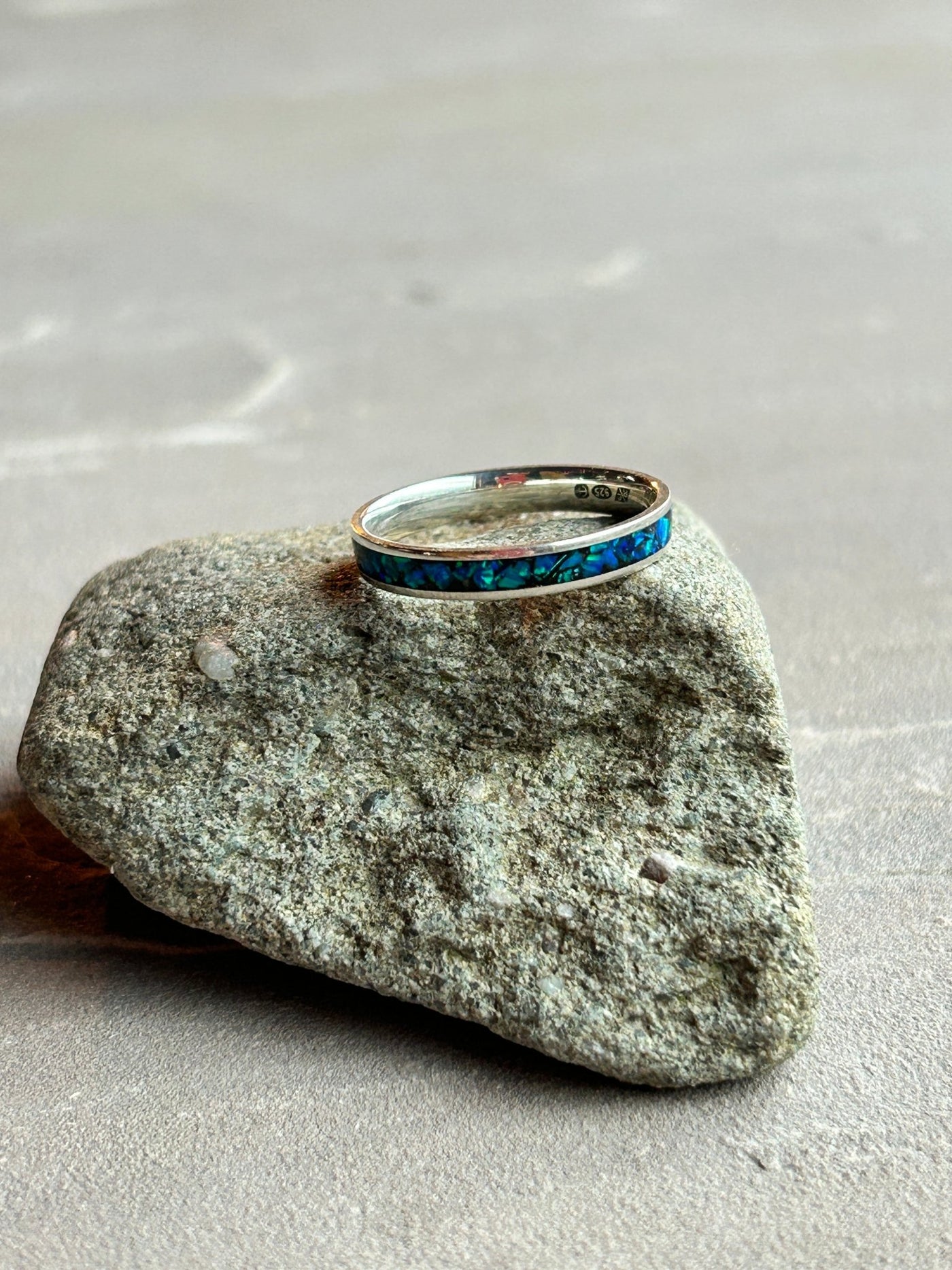 Silver inlay ring with cobalt blue opal inlay shown on a textured stone surface