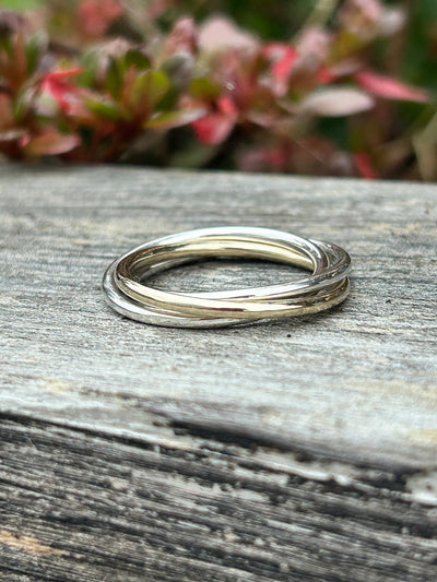 Silver interlocking ring on a wooden surface with blurred greenery in the background