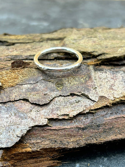 rounded silver stacking band with a hammered finish shown on a piece of bark
