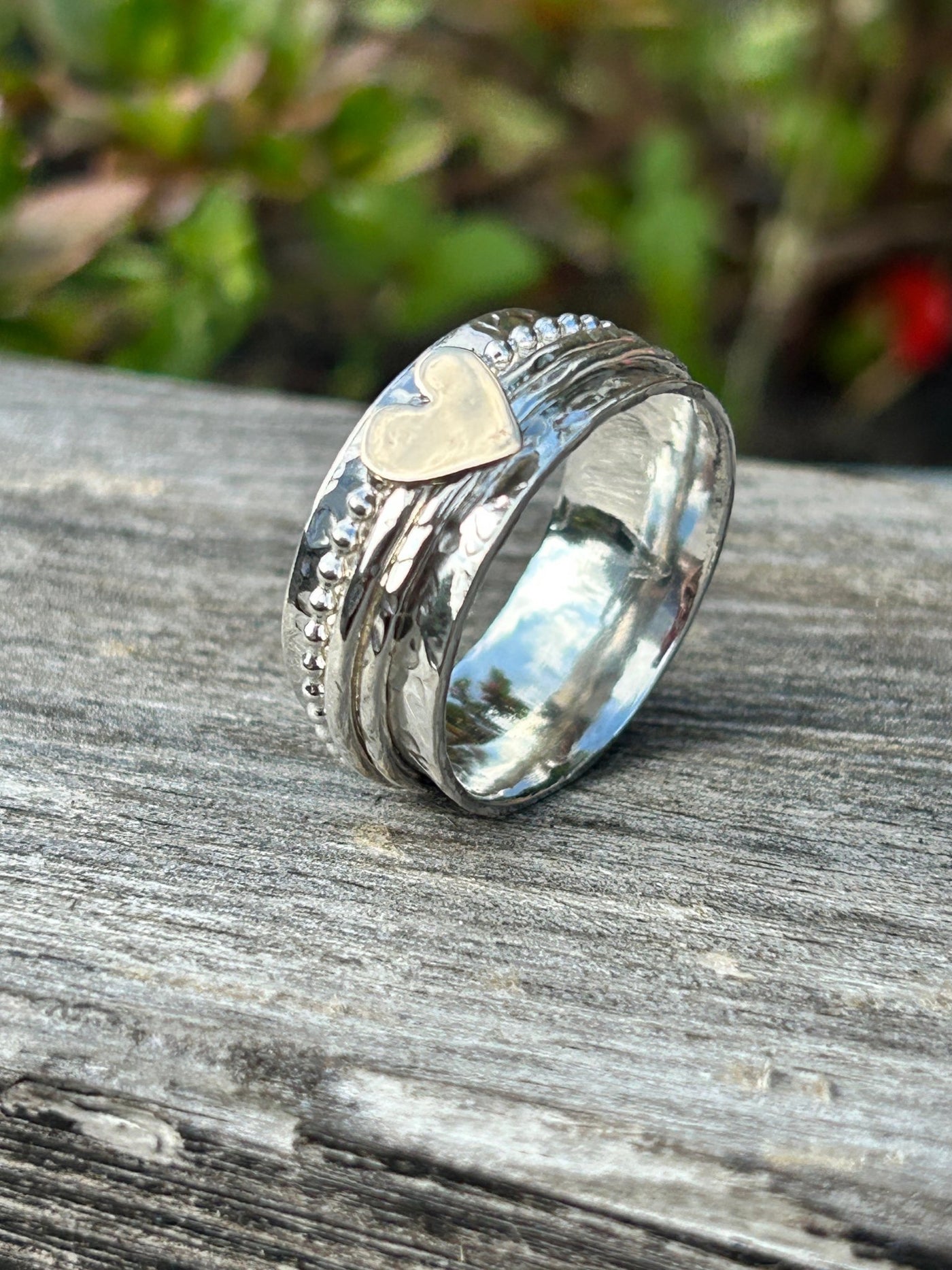 Sterling Silver Heart Spinner ring with three spinning bands one with a gold heart on a shelf and foliage on the background