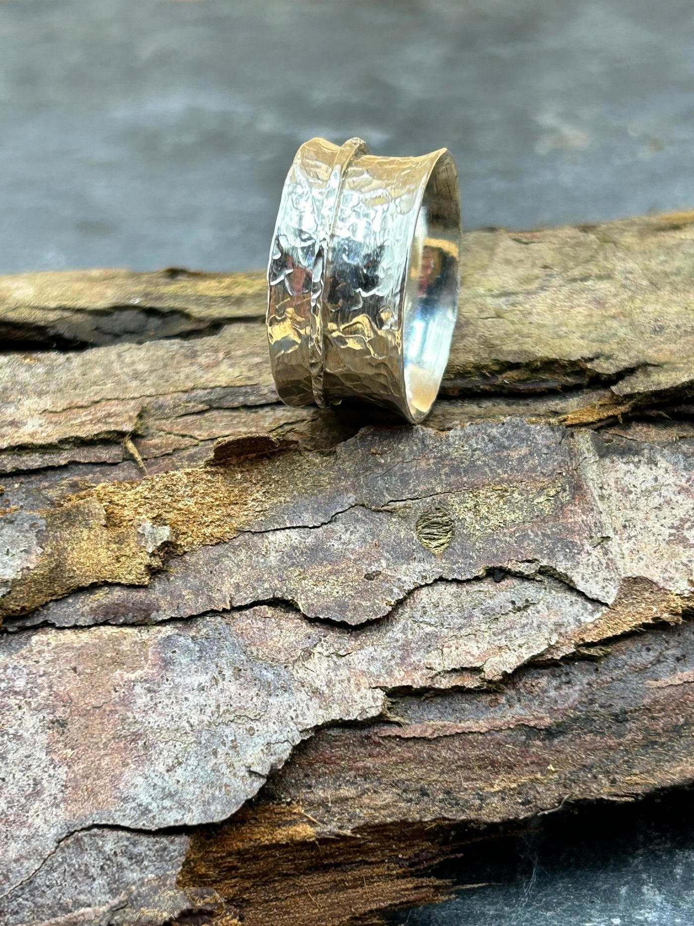 Wide Sterling silver spinner ring with one silver outer spinning band shown on a log