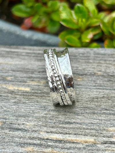 Silver spinner ring with three outer spinning bands on a wooden shelf and greenery in the background