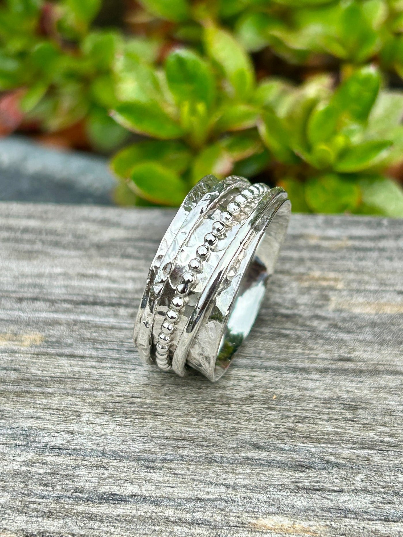 Silver spinner ring with three textured outer spinning bands on a wooden shelf and greenery in the background