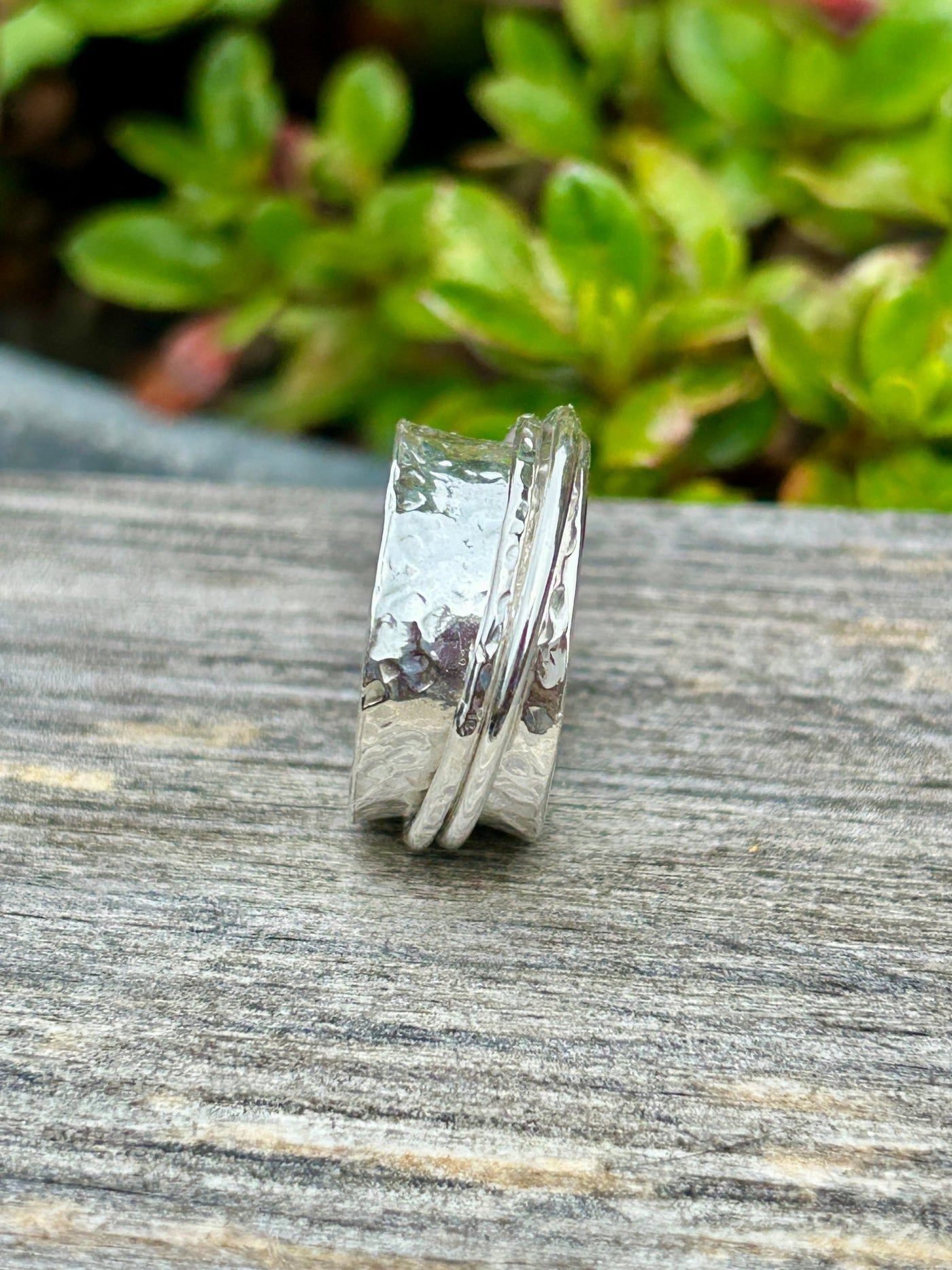 Sterling Silver spinner ring with two outer spinning bands on a wooden shelf and greenery in the background