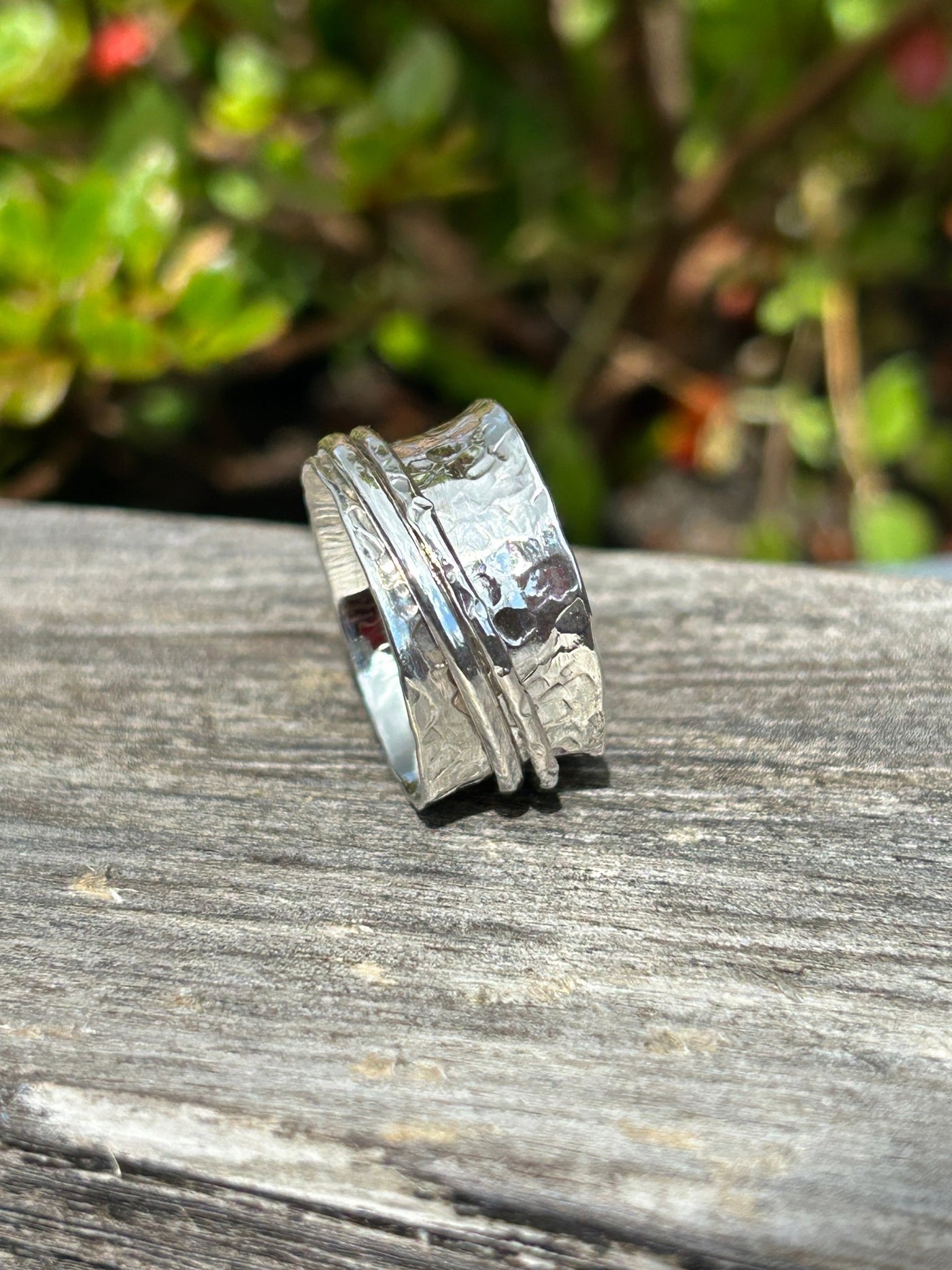 Silver spinner ring with two outer spinning bands on a wooden shelf and greenery in the background