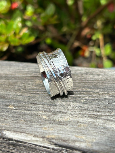 Silver spinner ring with two outer spinning bands on a wooden shelf and greenery in the background