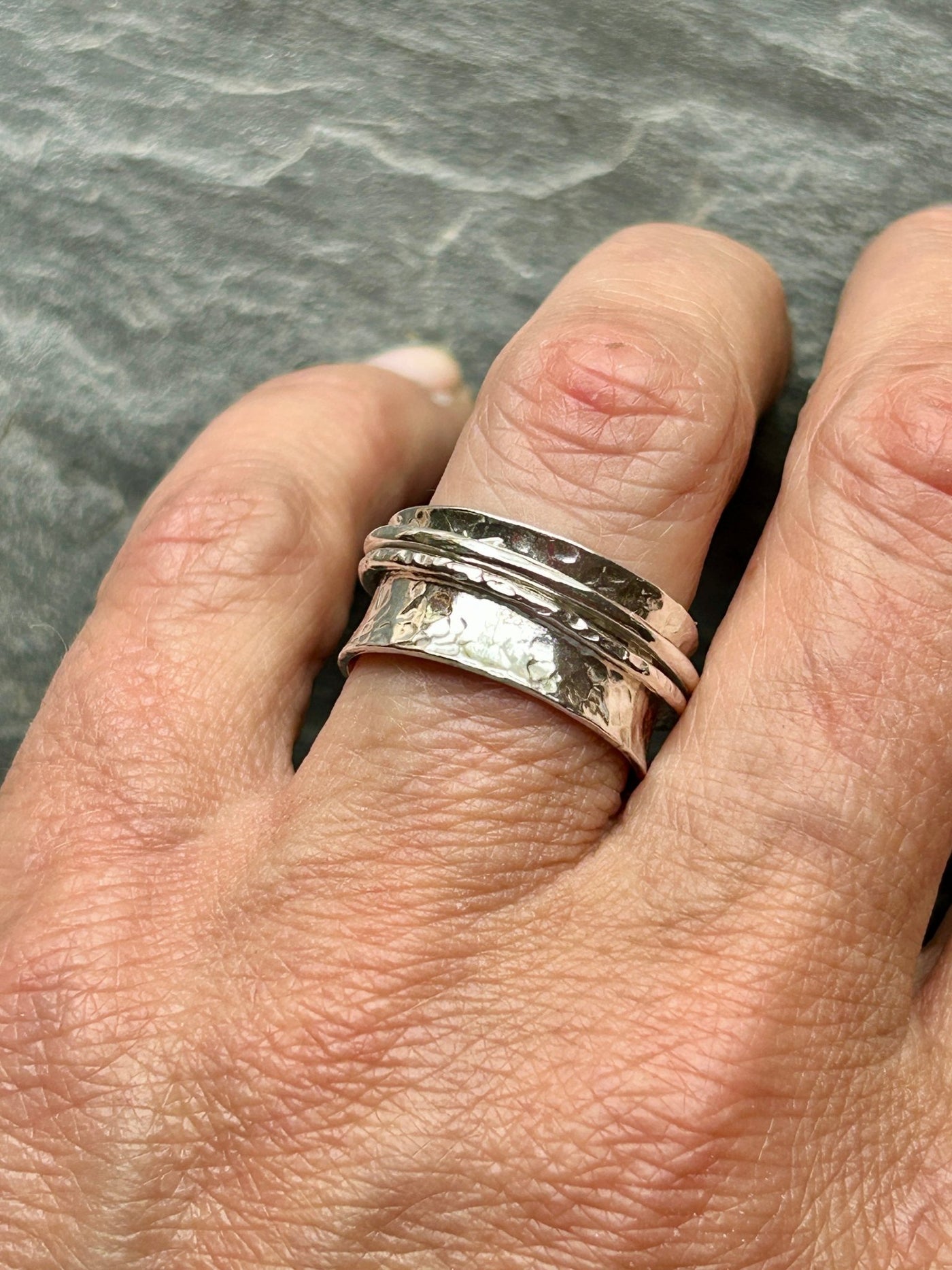Silver spinner ring on a finger with a textured band and two spinning outer bands against a gray background