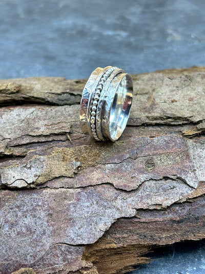 Silver spinner ring with three outer spinning bands on a piece of bark