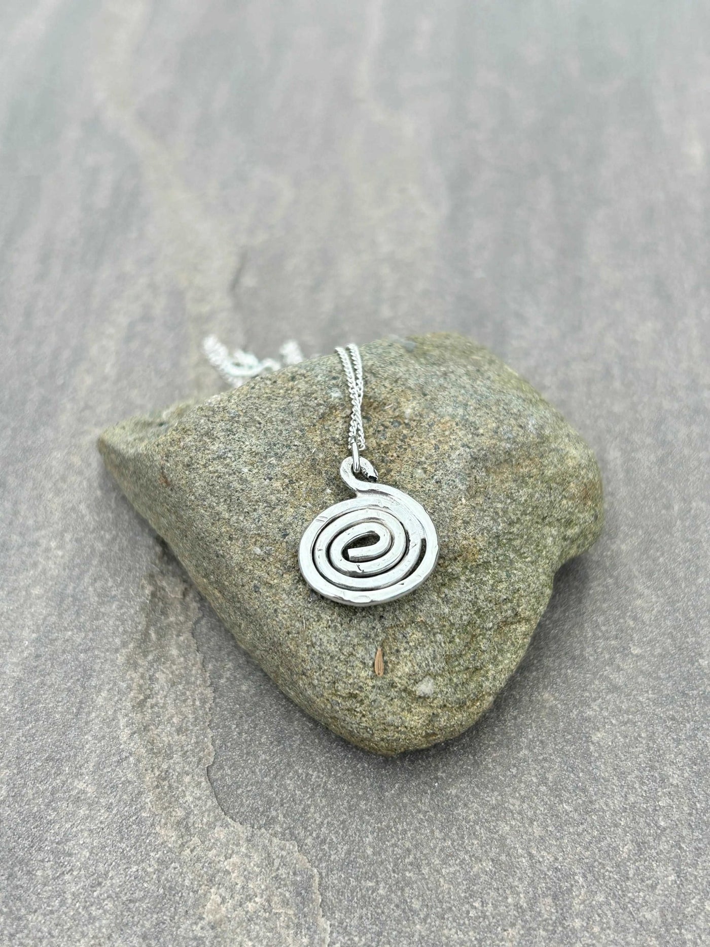 Small Spiral Silver pendant shown on a stone