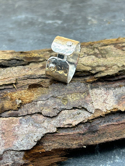 Hammered wide silver band ring with rivet detail and open front. Shown on a piece of wood
