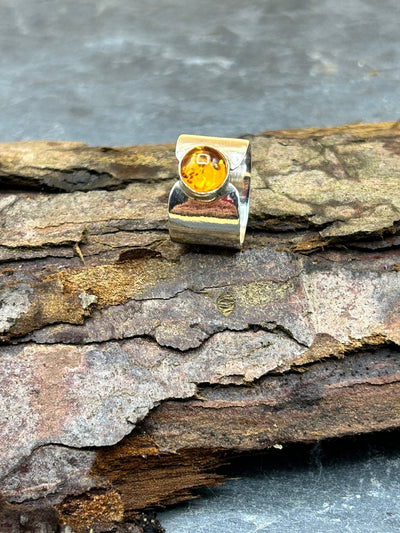 wide sterling silver band with an amber cabochon by LaVidaLoca Jewellery shown on a piece of wood